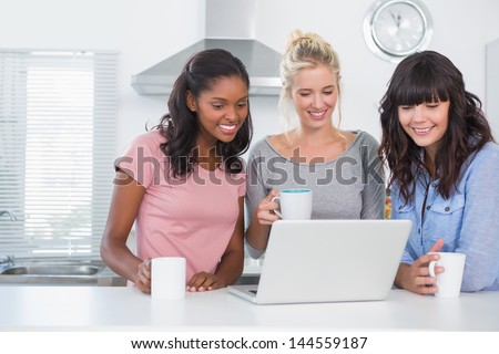 Pretty friends having coffee together and looking at laptop at home in kitchen