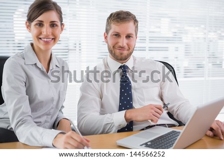 Business people smiling at camera with laptop sitting at desk in office