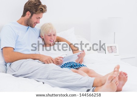 Handsome father and son using a tablet together in bed