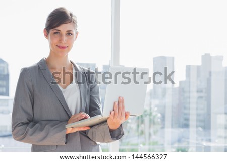 Businesswoman holding laptop by a large window