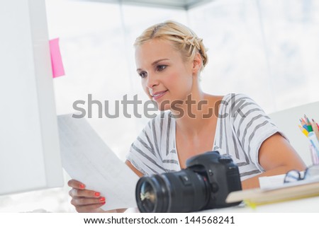 Pretty photo editor looking at a contact sheet with a digital camera on the desk