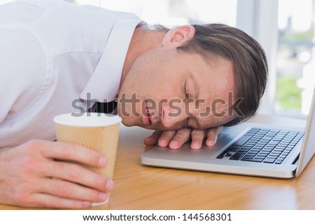 Businessman having a nap on his laptop while he is holding a cup of coffee