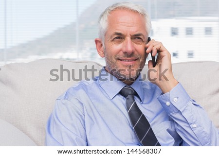 Cheerful businessman calling on smartphone on sofa in staffroom