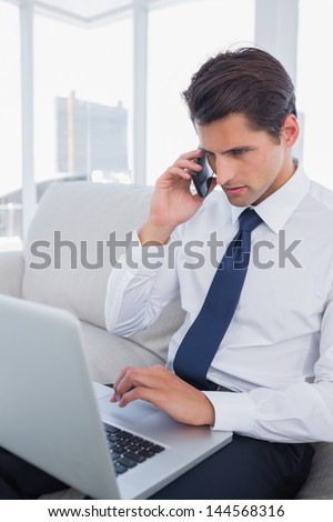 Businessman calling with his cell phone and using his laptop at the office