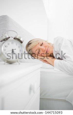 Blonde woman in bed asleep before her alarm goes off