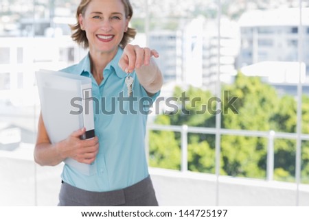Estate agent showing house keys and smiling at camera in a bright office