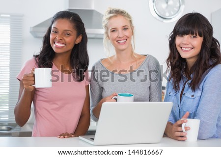 Happy friends having coffee together with laptop smiling at camera in kitchen