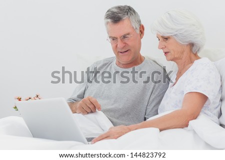 Man with wife pointing at a laptop in bed
