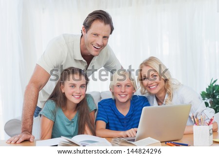 Smiling family using the laptop together to do homework in living room