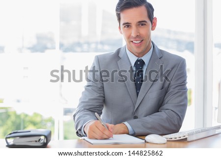 Smiling businessman writing at his desk in the office