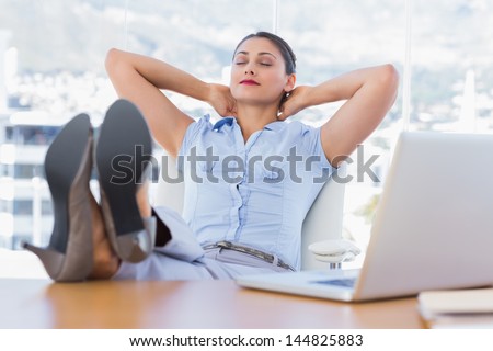 Attractive businesswoman relaxing in her office with her foot on the desk