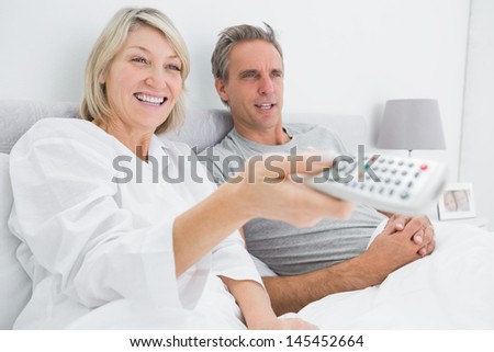 Happy couple watching tv in bed at home in bedroom