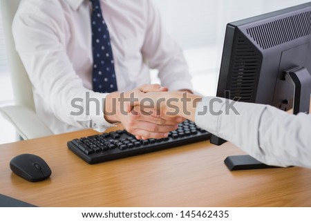 Businessman shaking hands with a co worker at his desk in office