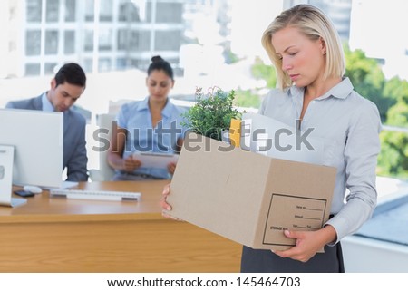 Sad businesswoman leaving office after being let go holding box of belongings