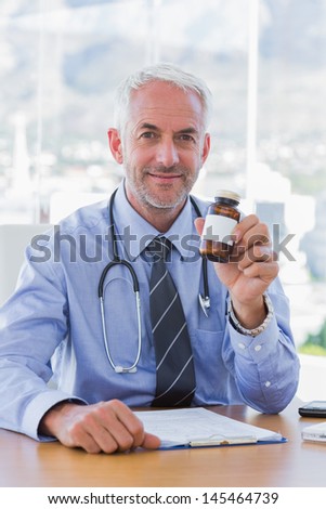 Attractive doctor holding medicine jar sitting behind his desk