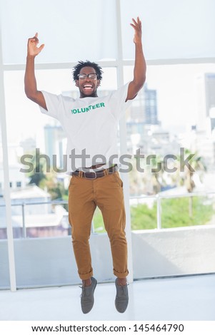 Man jumping with volunteer tshirt then raising his arms in a modern office