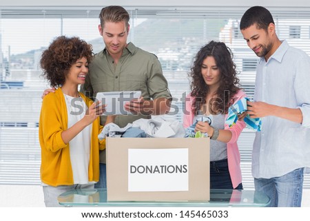 Volunteers using tablet and taking out clothes from a donation box for a charity