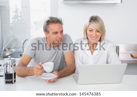 Happy couple using laptop in the morning sitting at kitchen counter