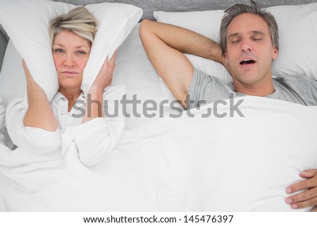 Man snoring loudly as partner blocks her ears at home in bedroom