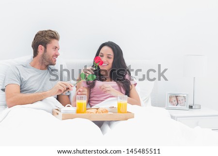 Pretty woman smelling a rose given by her husband during breakfast in the bed