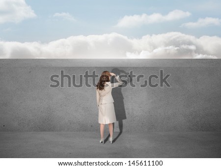 Businesswoman watching a grey wall with the sky in background