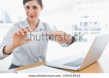 Young businesswoman pointing to blank business card at desk in office