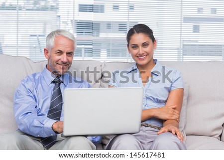 Business people with laptop smiling at camera on couch in staffroom