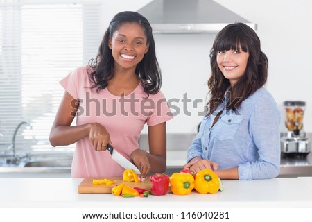 Cheerful friends preparing vegetables smiling at camera in kitchen
