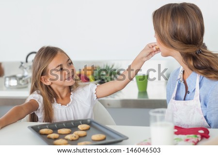 Young girl giving a cookie to her mother in the kitchen