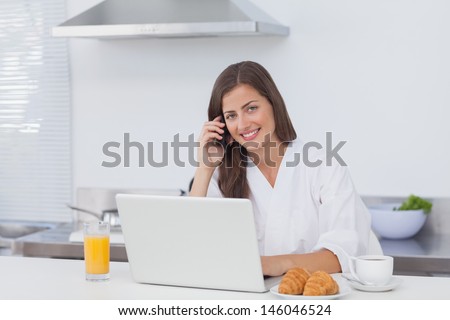 Woman phoning and using a laptop at the same time in the kitchen