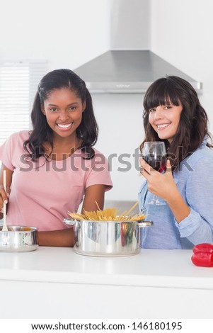 Smiling friends preparing dinner together in kitchen looking at camera