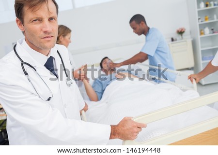 Serious doctor looking at the camera while medical team taking care of a patient