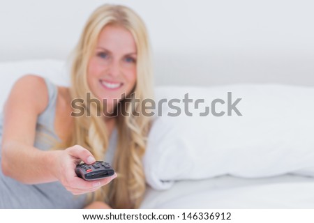 Woman pointing the remote control at the camera in her bed