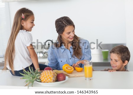 Attractive woman cutting an orange for her children in the kitchen