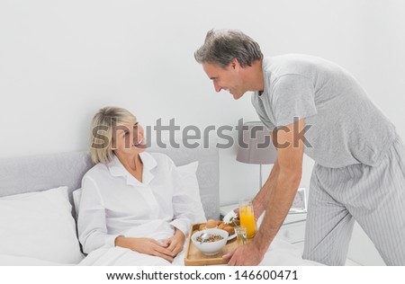 Caring man bringing breakfast in bed to his partner at home in bed