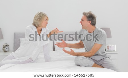 Couple arguing in bedroom sitting on bed