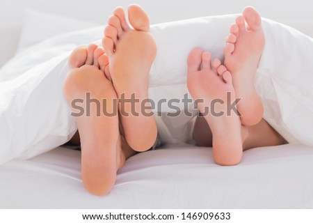 Couples feet crossed under the duvet in bed