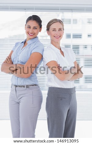 Cheerful businesswomen standing back to back with arms folded