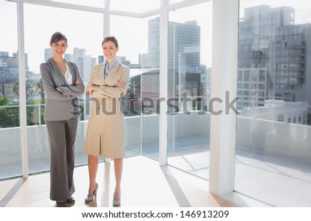 Smiling businesswomen standing in bright office with arms crossed
