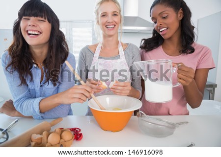 Laughing friends making pastry together at home in kitchen