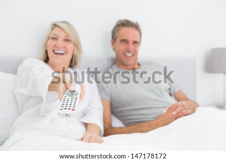 Laughing couple watching tv in bed at home in bedroom
