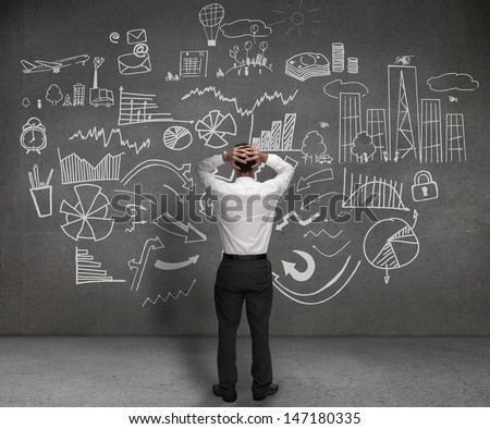 Stressed businessman looking at drawings of charts and sketches on a wall Stressed businessman looking at drawings of charts and sketches on a wall