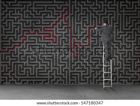 Businessman standing on a ladder and drawing a red line through black maze on a wall