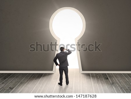 Businessman looking through a keyhole shape door in dark grey room