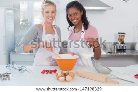 Young friends making pastry together looking at camera at home in kitchen
