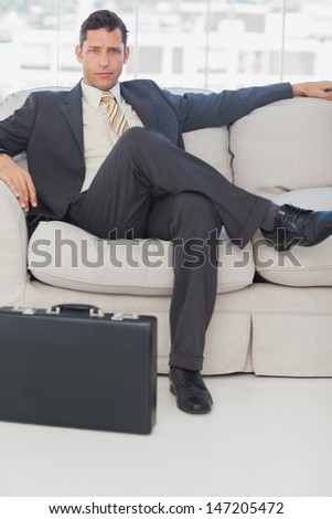 Serious businessman sitting with legs crossed on the couch with his briefcase