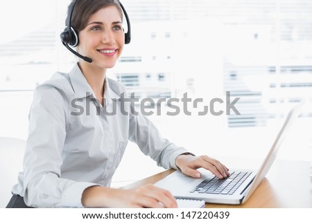 Smiling call center agent working at desk with headset and laptop
