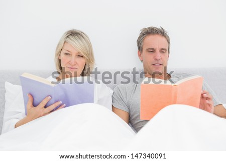Relaxed couple reading in bed at home in bedroom