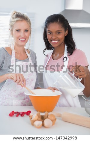 Smiling friends making dough together looking at camera at home in kitchen