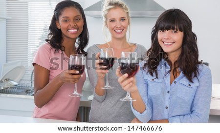 Happy friends enjoying glasses of red wine at home in kitchen smiling at camera